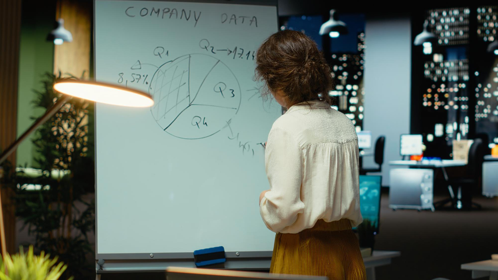 Woman writing on a whiteboard and looking at data.